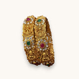 Pair of gold bangles with gemstones on a white background