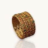 Gold bracelet with embedded red and green stones on a white background