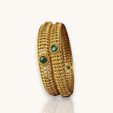 Gold bangles with green gemstones on a white background