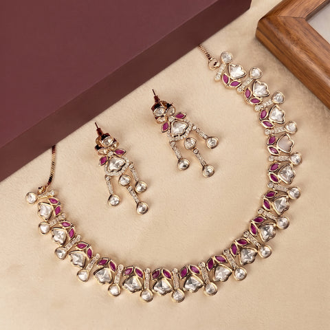 Gold-plated Indian Kundan jewelry set featuring a necklace, earrings, and a matching box, decorated with clear crystals and pink gemstones on a beige background.