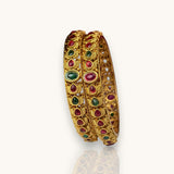 Pair of gold bangles with gemstones on a white background
