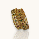 Gold bracelet with embedded red and green stones on a white background