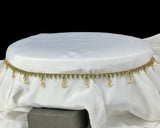 Decorative waist belt with green stones and gold accents on a white fabric background