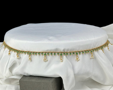 Decorative waist belt with green stones and gold accents on a white fabric background