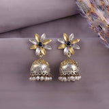 A pair of gold and silver flower-shaped jhumka earrings with black center stones and dangling pearl-like beads, displayed on a soft mauve fabric background.