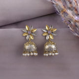 A pair of traditional Indian jhumka earrings with gold and silver floral studs, purple center stones, and dangling silver bell-shaped charms adorned with small white pearl beads, displayed on a textured mauve surface.