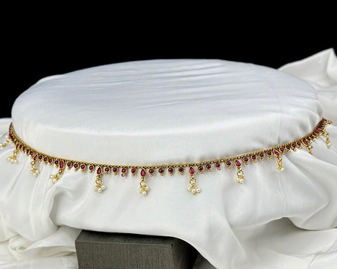 Decorative belt with red stones and gold accents on a white fabric background