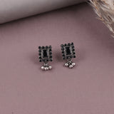A pair of rectangular silver-toned earrings with black rectangular center stones, surrounded by small black stones, and hanging silver bead drops, displayed on a dusty mauve surface.