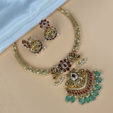 Gold jewelry set with red and green stones on a beige surface