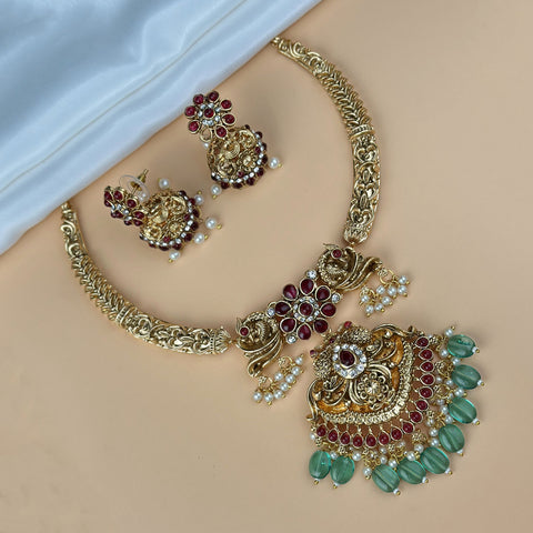 Gold jewelry set with red and green stones on a beige surface