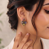 A close-up lifestyle shot of a woman wearing a silver-toned floral stud earring with multiple colorful gemstone accents (purple, yellow, orange, and green) on her earlobe.