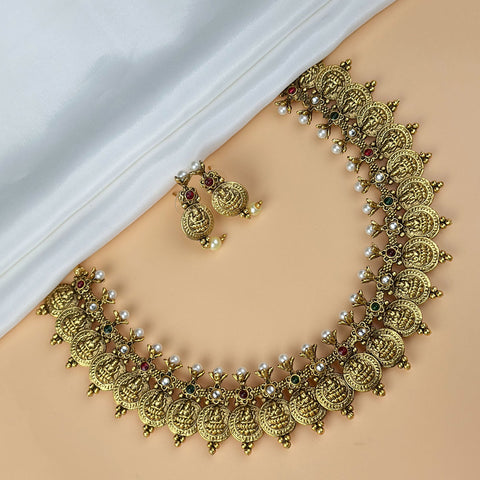 Gold necklace with intricate designs and pearl-like beads on a beige surface.