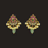 A pair of gold-plated Indian chandelier earrings featuring pink and green enamel details, clear crystal accents, and dangling pearl-like beads with green teardrop charms, set against a solid black background.