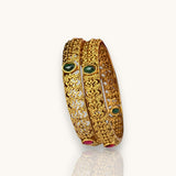 Gold bangles with green gemstones on a white background