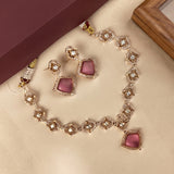 Gold-plated jewelry set featuring a necklace and matching earrings with pink stone accents and clear rhinestone details, displayed on a beige surface with a maroon box in the background.