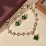 Gold-plated jewelry set featuring a necklace, earrings, and bracelet with square-cut green stones surrounded by clear crystals, displayed on a cream satin surface.