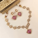 Gold-plated Indian jewelry set featuring a necklace and matching earrings with pink stone accents and clear rhinestones, displayed on a cream surface next to an ornate decorative box.