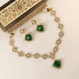 Gold-plated Indian style jewelry set featuring a necklace and matching earrings with green stone accents, displayed on a cream-colored surface next to an ornate decorative box.