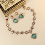 A traditional Indian jewelry set featuring a necklace, earrings, and a decorative box. The jewelry has mint green stone inlays surrounded by rose gold settings with clear crystals, and small red and gold bead accents.