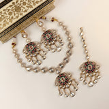Gold-toned Indian jewelry set featuring a necklace, matching earrings, and a choker with clear teardrop stones and red and green enamel accents, displayed on a cream background with a decorative box corner visible.