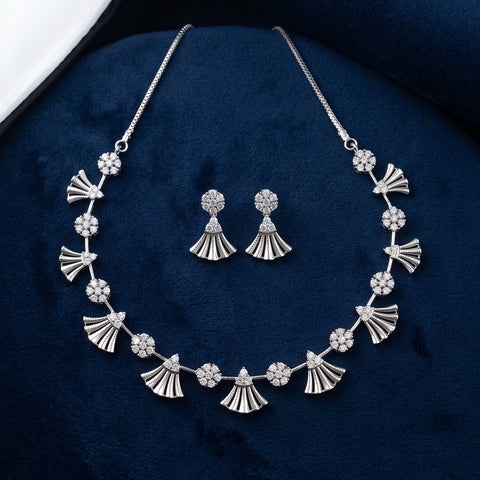 Silver-tone jewelry set featuring a necklace and matching drop earrings with fan-shaped and floral motifs set with clear stones, displayed on a dark blue velvet surface.