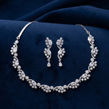 Silver floral jewelry set with a matching necklace and drop earrings, featuring clear rhinestones, displayed on a dark navy blue velvet fabric background.