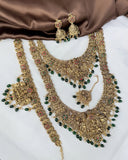 Ornate gold necklace with green beads and matching earrings on a brown fabric background