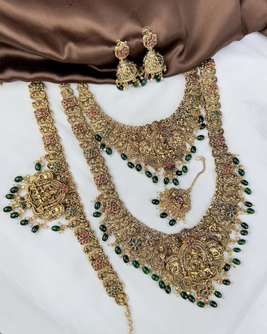 Ornate gold necklace with green beads and matching earrings on a brown fabric background