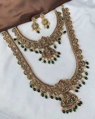 Ornate gold necklace with green beads and matching earrings on a white surface.