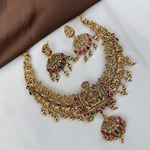 Gold necklace with red and green gemstones on a white surface