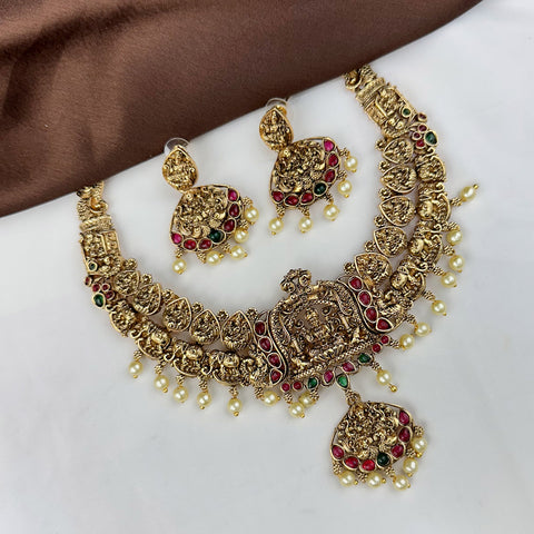 Gold necklace with red and green gemstones on a white surface