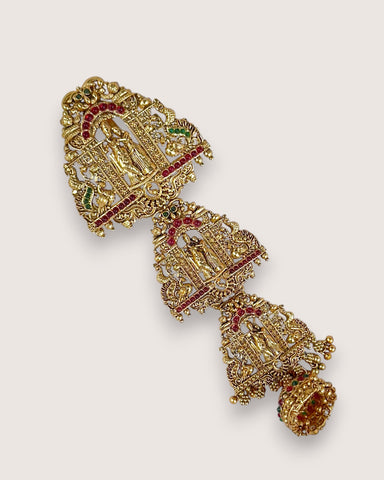 Decorative gold earring with red and green gemstones on a light gray background