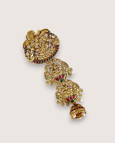 Gold earrings with intricate designs and red and green gemstones on a light gray background