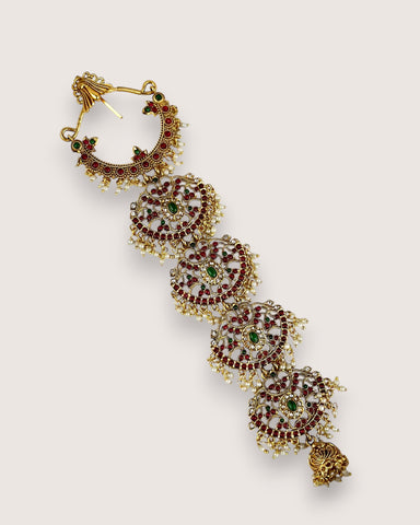 Ornate gold earrings with red and green gemstones on a light gray background