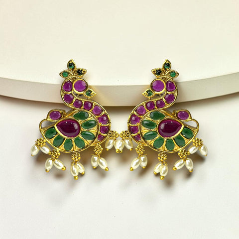 Ornate gold earrings with purple and green gemstones on a white background