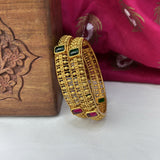 Gold bracelet with gemstones on a white surface with a wooden box and pink fabric in the background