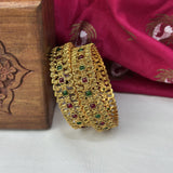 Gold bangles with gemstones on a white surface with a wooden box and pink fabric in the background.