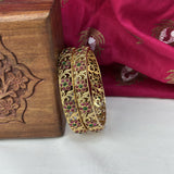 Gold bangles with gemstones on a wooden box and pink fabric background