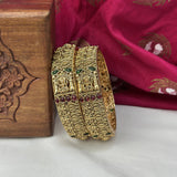 Gold bangles with intricate designs on a pink fabric background