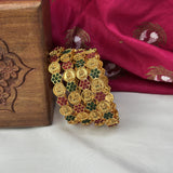 Gold bracelet with gemstones on a white surface with a wooden box and red fabric in the background