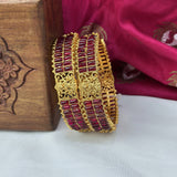 Gold and red bracelet on a white surface with a wooden box and pink fabric in the background