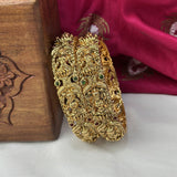 Decorative gold bangle with green gemstones on a wooden box and red fabric background