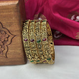 Gold bangles with gemstones on a wooden box and pink fabric background