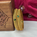 Gold bangles with green stones on a wooden box