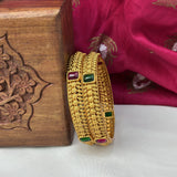Gold bangles with gemstones on a wooden box and pink fabric background