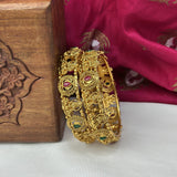Gold bangles with gemstones on a wooden box and pink fabric background