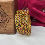 Set of gold bangles with gemstones on a wooden box and pink fabric background