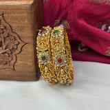 Gold bracelet with gemstones on a white surface with a wooden box and pink fabric in the background