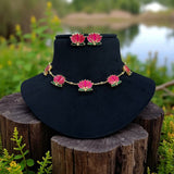 Necklace and earrings with pink floral designs on a black stand against a natural background.