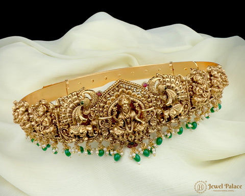 Decorative gold belt with green beads on a white fabric background